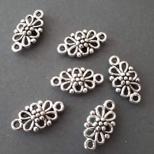 Puede incluir: Seis abalorios conectores de metal plateado en forma de flor con un bucle en cada extremo. Los abalorios están diseñados con un delicado patrón floral y una pequeña perla en el centro de cada flor.