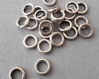 May include: A pile of silver jump rings, a type of jewelry finding, on a gray fabric background.