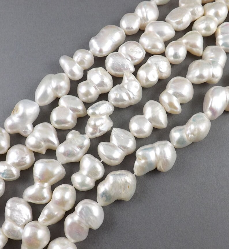 May include: A strand of white baroque pearls, each pearl is unique in shape and size. The pearls have an iridescent sheen and are strung on a white thread.