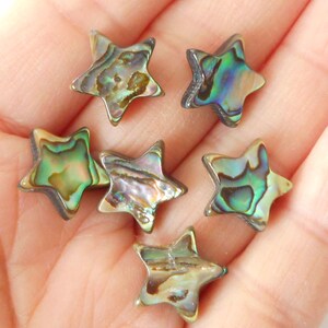 K&ouml;nnte beinhalten: Sechs sternf&ouml;rmige Perlen aus irisierendem Abalone-Muschelschalen. Die Perlen sind in einem Mix aus Gr&uuml;n, Braun und Gold.