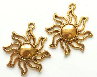 May include: Two gold-toned metal sun charm pendants with a raised center circle. The charms have a detailed design with wavy rays emanating from the center circle.