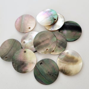 Może przedstawiać: Kolekcja okrągłych, tęczowych czarnych i brązowych dysków z muszli perłowej z otworem w środku. Dyski mają średnicę około 5 cm.