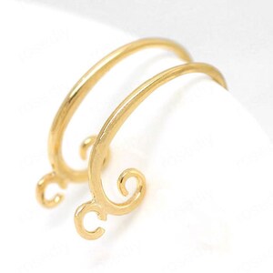 May include: Two gold-colored earring findings with a curved design. Each finding has a loop at the bottom and a decorative swirl at the end of the curved top. The earrings are set against a white background.