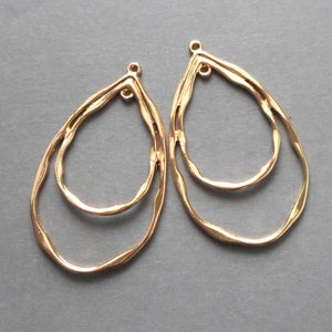May include: Two gold-colored, teardrop-shaped earring pendants. Each pendant features a double-layered design with a textured, wavy surface. The pendants have small loops at the top for attachment, ideal for jewelry making.
