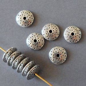 Könnte beinhalten: Silberne Metallperlen mit einer strukturierten Oberfläche, die an einen Seeigel erinnern. Die Perlen sind in einer Reihe angeordnet, wobei einige Perlen übereinander gestapelt sind.