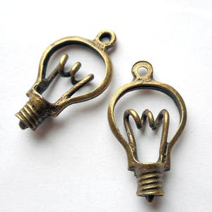 Op de afbeelding: Twee antieke goudkleurige metalen lichtbollen met een gedetailleerd filamentontwerp. De bedels hebben een lus aan de bovenkant om aan sieraden of andere knutselwerken te bevestigen.