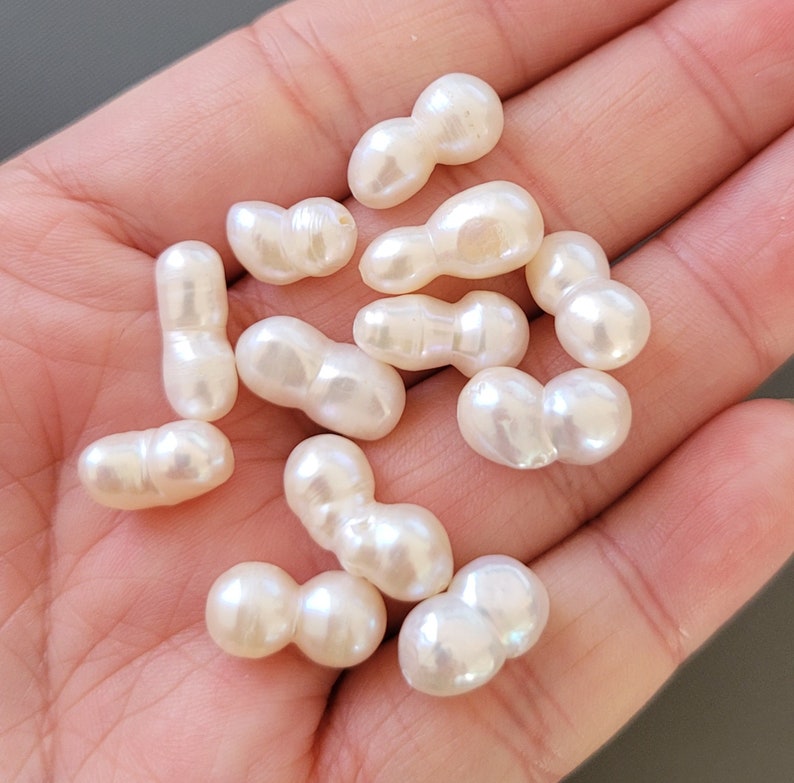 May include: A collection of white baroque pearl beads, each bead is a double pearl with an irregular shape.