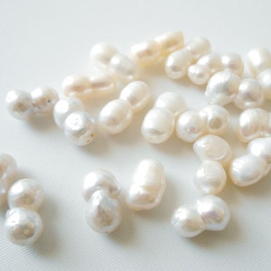 May include: A collection of white baroque pearls, each with an irregular shape and a slightly off-white hue. The pearls are arranged on a white surface.