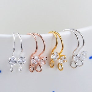 May include: Three pairs of earring findings with a clear crystal design. The findings are available in silver, rose gold, and gold.