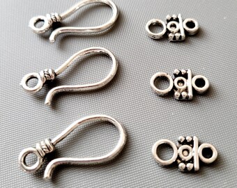 May include: Three silver earring hooks and three silver earring closures. The hooks are shaped like a teardrop with a small loop at the top. The closures are small and have a decorative design.