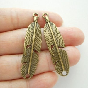 May include: Two antique gold-toned metal feather charms with a detailed design. Each charm has two holes for attaching to jewellery or crafts.