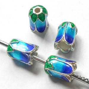 May include: Four enameled flower beads in shades of blue and green with silver-colored metal accents. The beads are strung on a silver-colored wire. The beads are designed to look like flowers.