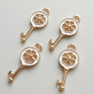 May include: Four gold key charms with white enamel flower designs. The keys have a simple, elegant design.