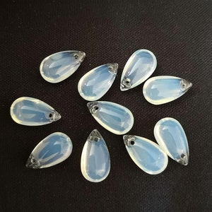 May include: A group of ten teardrop-shaped, iridescent, white glass beads with a hole at the top for stringing.