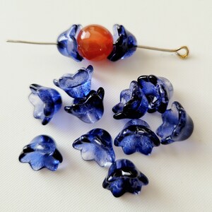 May include: A collection of blue glass flower beads, some strung on a wire with an orange bead in the center. The beads are translucent and have a slightly iridescent finish.