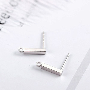 May include: Two silver earring posts with a small rectangular bar attached to the top. The posts are straight and the bars are perpendicular to the posts.