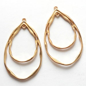 May include: Two gold-colored, teardrop-shaped earring components. Each component features a double-layered design with a textured, wavy outline. The top of each earring has a small loop for attachment. The earrings are set against a white background.