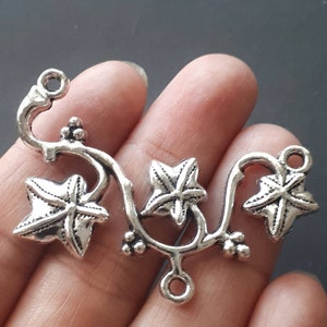 May include: Silver-toned metal charm featuring a vine with three five-pointed leaves. The charm has two loops for attaching to jewelry or other crafts.