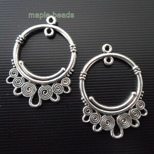 May include: Two silver hoop earrings with a decorative design of swirls and loops hanging from the bottom of each hoop.