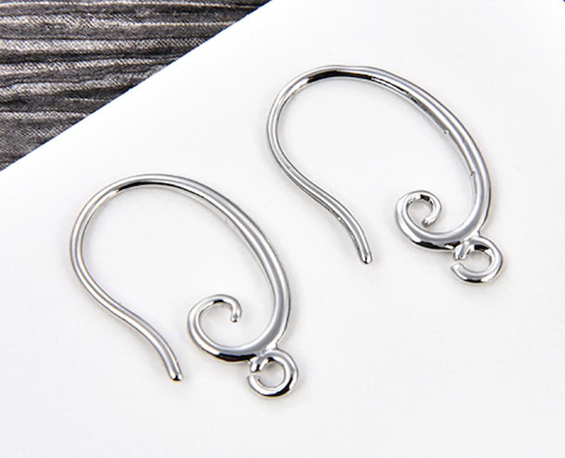 May include: Two silver-colored earring hooks. Each hook has a curved design with a looped end and a decorative swirl. The hooks are designed for jewelry making and are displayed against a white background.