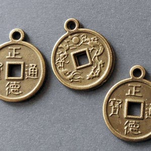 Può includere: Tre monete cinesi antiche color oro con un foro quadrato al centro. Ogni moneta presenta caratteri cinesi sul davanti e un disegno di drago sul retro.