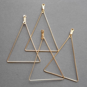 May include: Four gold-colored triangle-shaped earring components. Each component has a loop at the top for attachment. The triangles vary in size and are made of thin wire.