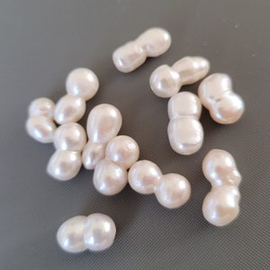 May include: A collection of off-white baroque pearls, each with an irregular shape and a smooth, glossy finish. The pearls are arranged on a gray surface.
