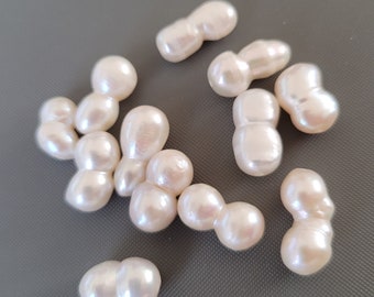 May include: A collection of off-white baroque pearls, each with an irregular shape and a smooth, glossy finish. The pearls are arranged on a grey surface.