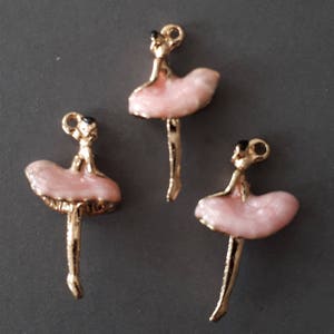 May include: Three gold-tone ballerina charms with pink skirts and black eyes. The charms are ideal for jewellery making or adding a touch of whimsy to crafts.