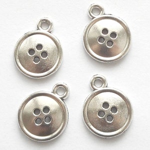 May include: Four silver metal button charms with four holes each. The charms have a shiny finish and are perfect for adding a vintage touch to jewellery or crafts.
