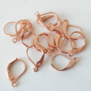 May include: A close-up of ten rose gold earring hooks. The hooks are made of metal and have a spring-loaded clasp.