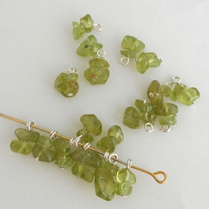 Può includere: Una collezione di perline di peridoto verde con anelli a salto d'argento. Alcune perline sono infilate su un filo d'oro.