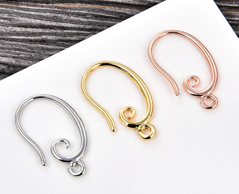 May include: Three metal earring hooks in silver, gold, and rose gold. Each hook has a curved design with a looped end for attaching earrings. The hooks are displayed on a white surface.