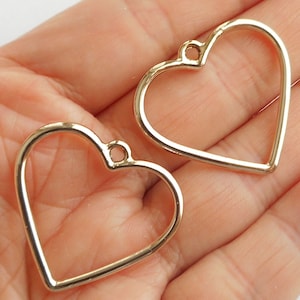 以下が含まれることがあります： 吊り下げまたは取り付け用の小さなループが上部にある、2つの金色の金属製のハート型のフレームです。