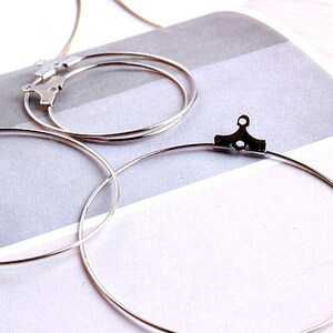 May include: Three silver hoop earrings of different sizes. The largest hoop has a silver clasp.