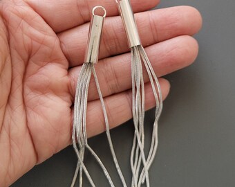 May include: Two silver chain tassel earrings with a cylindrical top. The tassels are made of multiple thin chains.