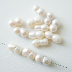May include: A collection of white baroque pearls, some are strung on a thin wire. The pearls are irregular in shape and have a smooth, glossy finish.