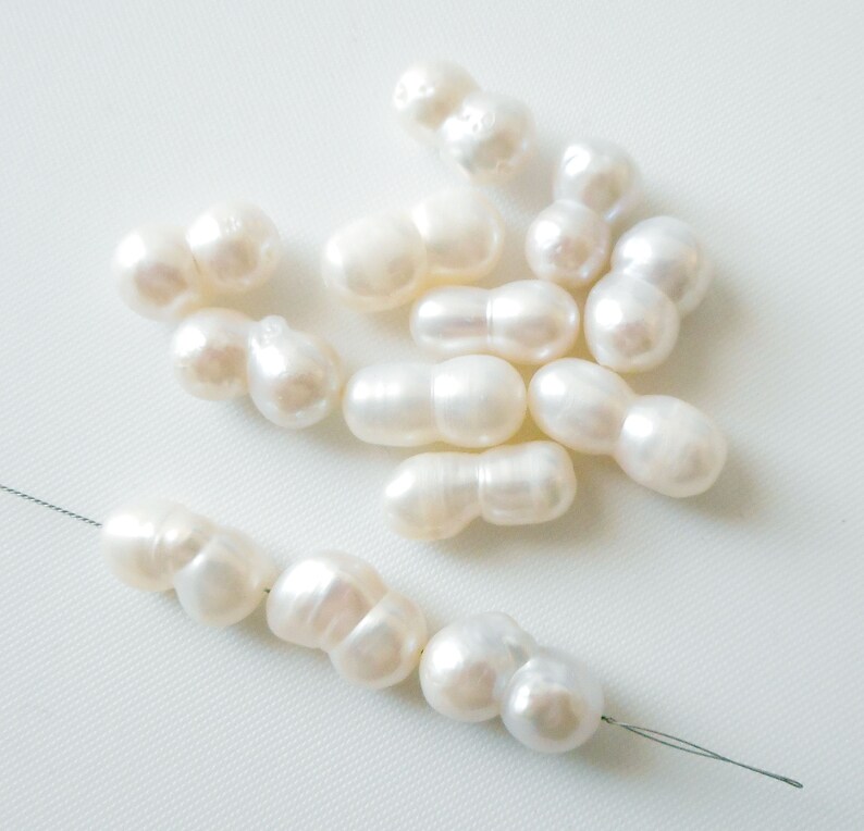 May include: A collection of white baroque pearls, some are strung on a thin wire. The pearls are irregular in shape and have a smooth, glossy finish.