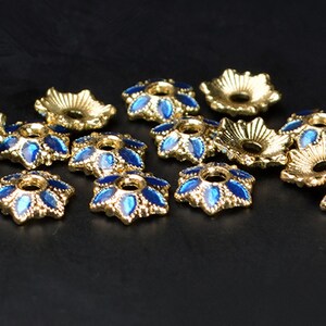 May include: A group of gold-colored metal bead caps with blue enamel accents. The caps have a starburst design and a hole in the center.