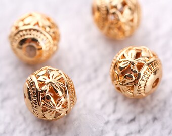 May include: Four gold-colored metal beads with intricate floral designs. The beads are round and have a hollow center.