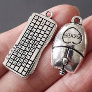 Pode incluir: Dois pingentes de prata, um com a forma de um teclado de computador com as teclas etiquetadas, e o outro com a forma de um rato de computador com a palavra "LOVE" na parte superior.