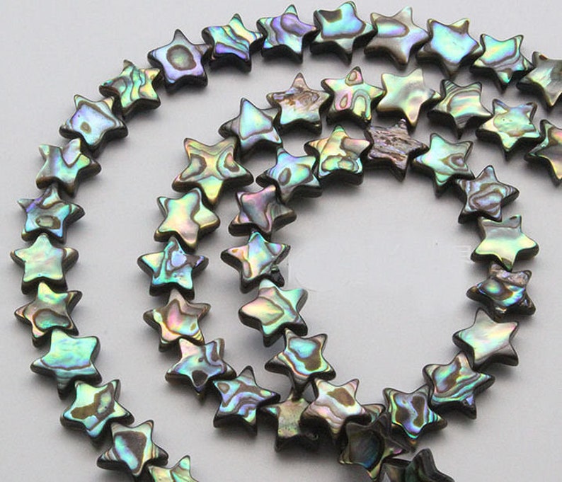 K&ouml;nnte beinhalten: Eine Str&auml;hne aus irisierenden Abalone-Muschelperlen in Sternform. Die Perlen sind in einem Mix aus Gr&uuml;n, Blau und Braun.