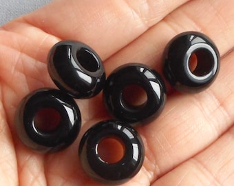 May include: Six glossy, black donut-shaped beads. Each bead has a smooth, reflective surface and a large, central hole. The beads are arranged in a hand, showcasing their polished appearance and potential for jewelry making or crafting projects.