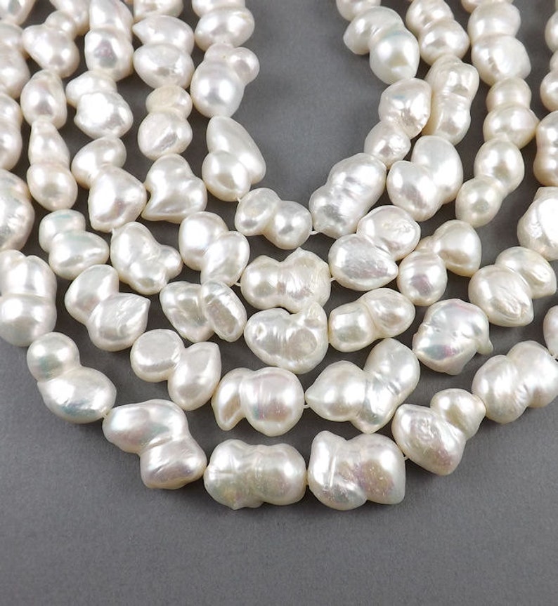 May include: A strand of white baroque pearls, with an iridescent sheen. The pearls are irregular in shape and size, and are strung on a clear thread.