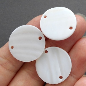 May include: Three white round shell beads with two holes each. The beads have a subtle striated pattern.