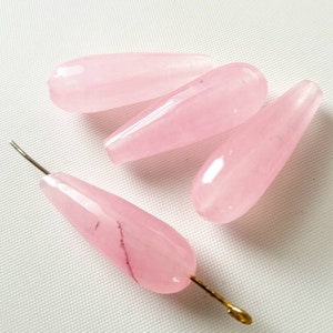 May include: Four pink teardrop-shaped beads with a smooth, polished finish. The beads are made of natural stone and have a translucent appearance.