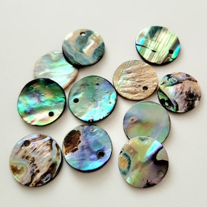 Könnte beinhalten: Sortiment aus irisierenden Abalone-Muschel-Runden-Scheiben-Anhängern mit einem Loch in der Mitte. Die Anhänger sind in verschiedenen Grüntönen, Blau- und Brauntönen.