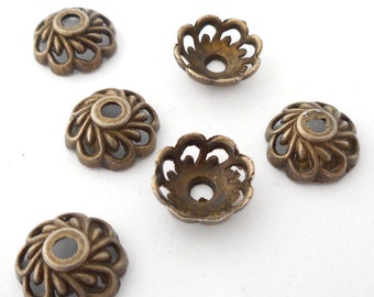 May include: Six antique gold-toned metal bead caps with a decorative, intricate, floral design. The caps are round and have a small hole in the center.