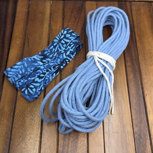 May include: A bundle of light blue rope tied with white string next to a folded blue fabric with a leaf pattern. The items are on a wooden surface.