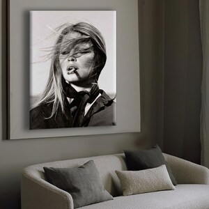 Puede incluir: Retrato en blanco y negro de una mujer con el pelo largo al viento, fumando un cigarrillo. Lleva un top oscuro y una bufanda. La imagen enmarcada est&aacute; montada en una pared sobre un sof&aacute; con cojines.